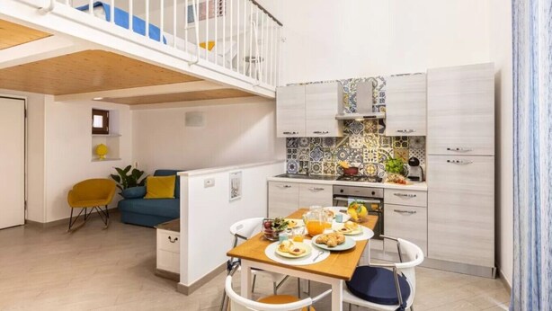 A compact kitchen with a dining area, a small seating space, and a staircase leading to an upper level. - Cosy House Under The Arches In Sorrento Old Town (Sorrento)