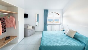 A modern bedroom with a bed, a grey sofa, a wardrobe, and a window with a view.