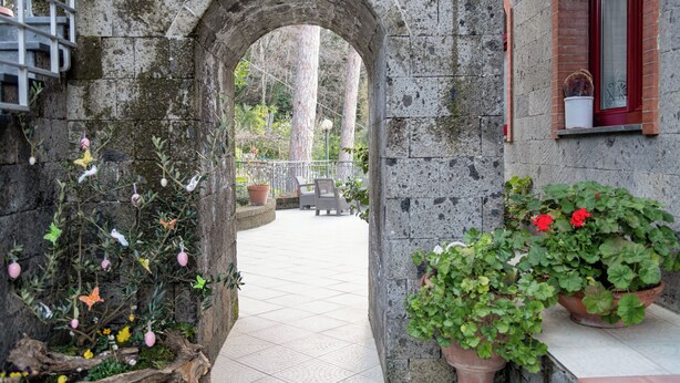 An arched stone doorway leading to a tiled patio area with potted plants and outdoor furniture.