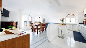 A modern kitchen with white cabinets, a dining area with wooden chairs, and a TV mounted on the wall.