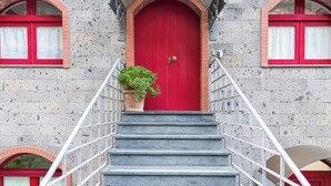 A building with a red door, a staircase with metal railings, and a potted plant on the steps.