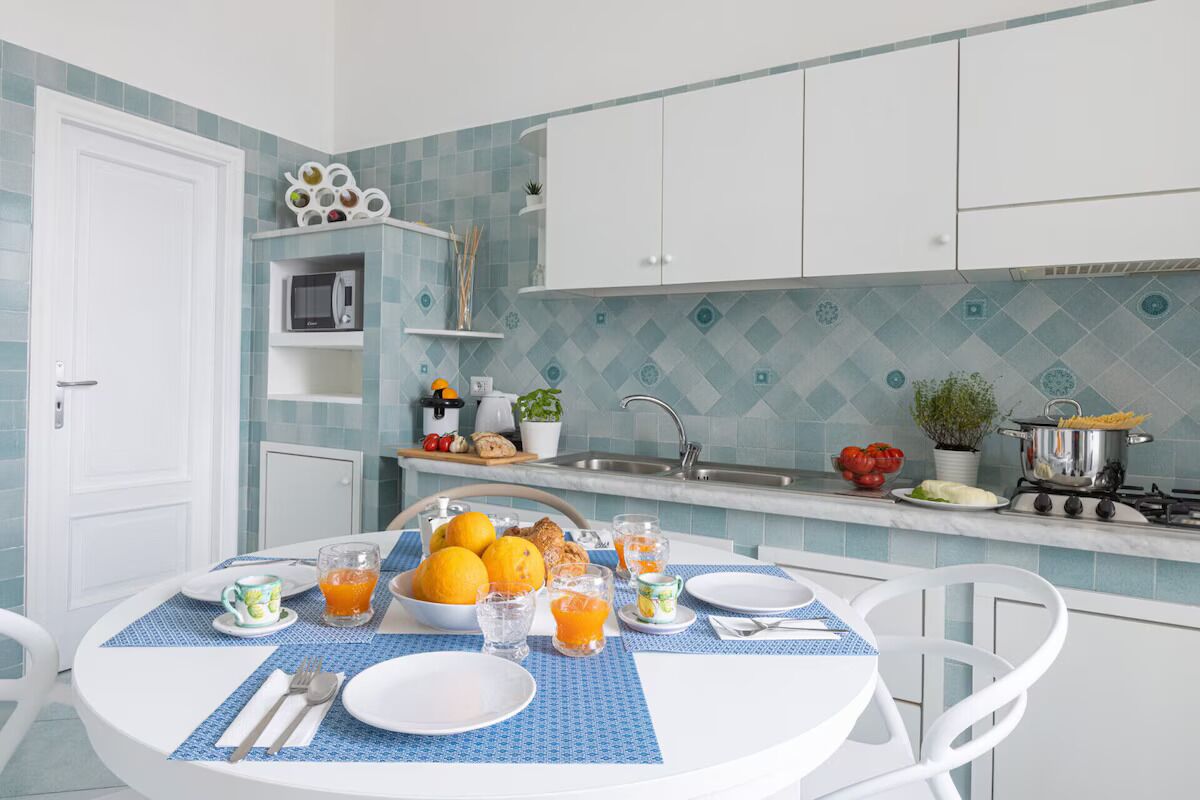 A modern kitchen with a breakfast setup including a table with plates, glasses, and a bowl of oranges.