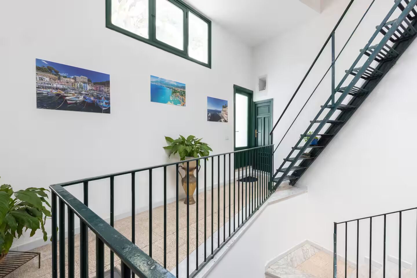 A staircase with black railings, a potted plant, and three framed pictures on the wall.