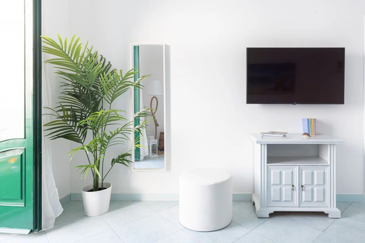 A living room with a large flat-screen TV mounted on the wall, a white cabinet with a mirror, and a potted plant.