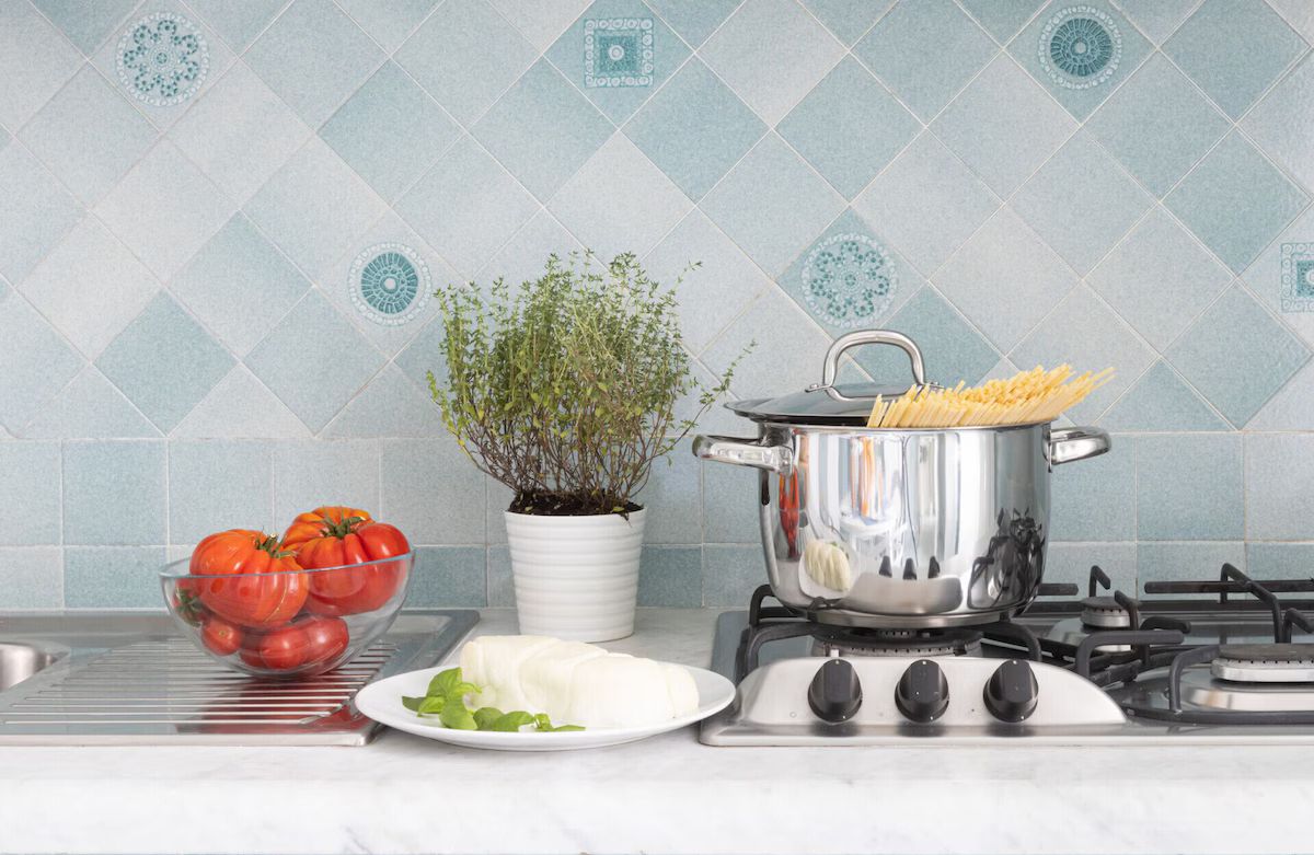 A kitchen with a pot of boiling water, a bowl of tomatoes, a plate of cheese, and a potted plant.