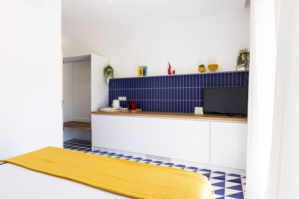 A compact kitchen with a blue tiled backsplash, a wooden countertop, and a television.
