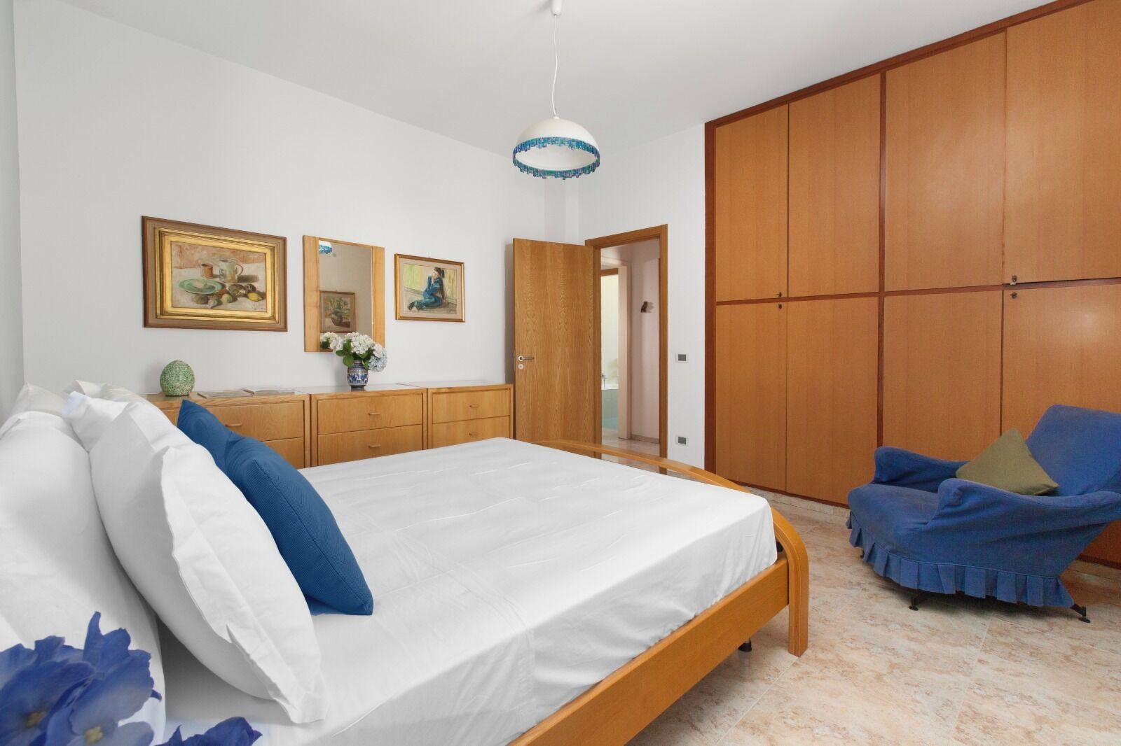 Un dormitorio con una cama grande, un armario de madera y un sillón azul.