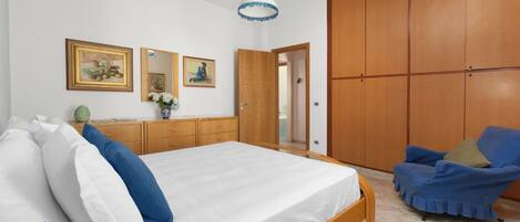 Un dormitorio con una cama grande, un armario de madera y un sillón azul.