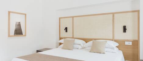 A hotel room with a large bed, a wooden headboard, a bedside table, and a framed picture on the wall.