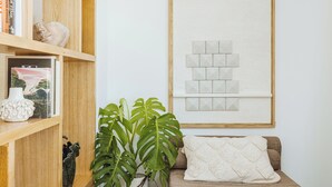 A living room with a wooden bookshelf, a large plant, a framed abstract art piece, and a beige sofa with a white throw pillow. - Exclusive Suite With Terrace By Sorrento Main Square (Sorrento)