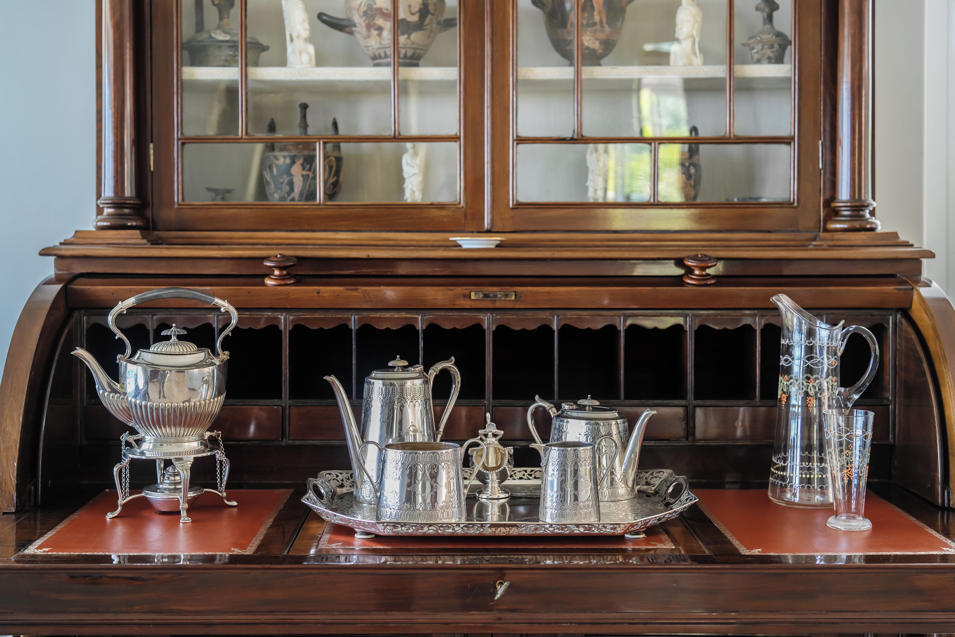 A wooden table with a tray holding a silver tea set, including a teapot, cups, and a sugar bowl.