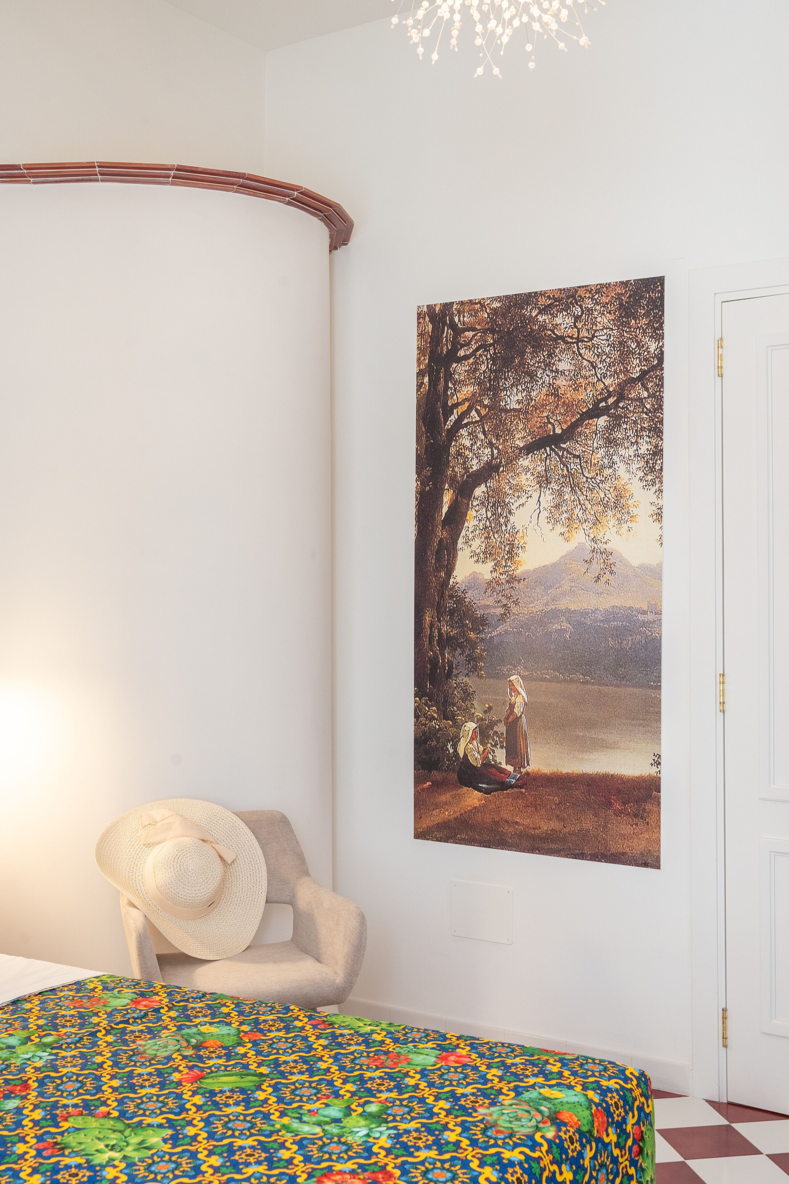 A room with a bed, a chair, a painting, and a door.