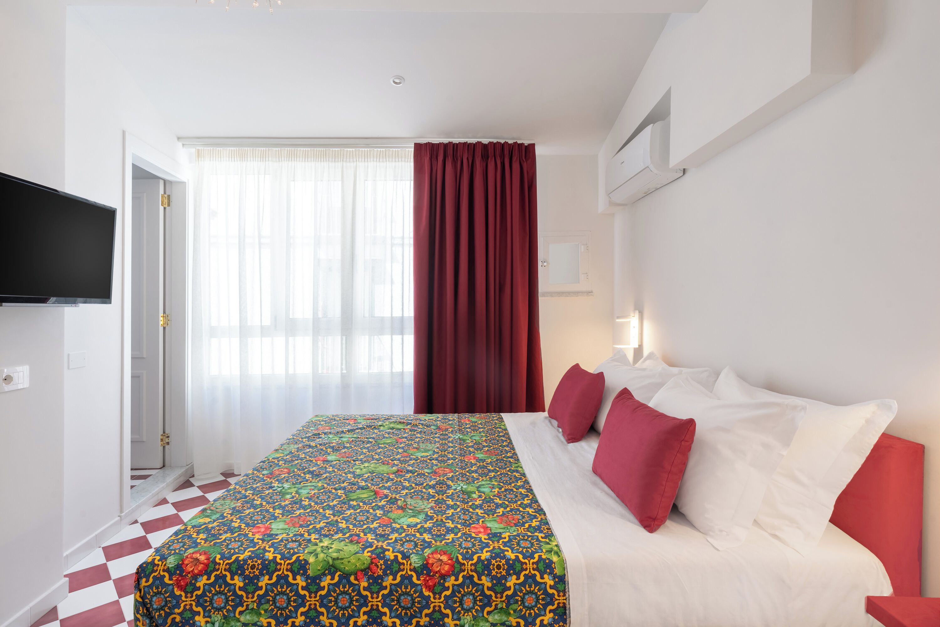 A hotel room with a bed, a TV, a window with curtains, and a checkered floor.