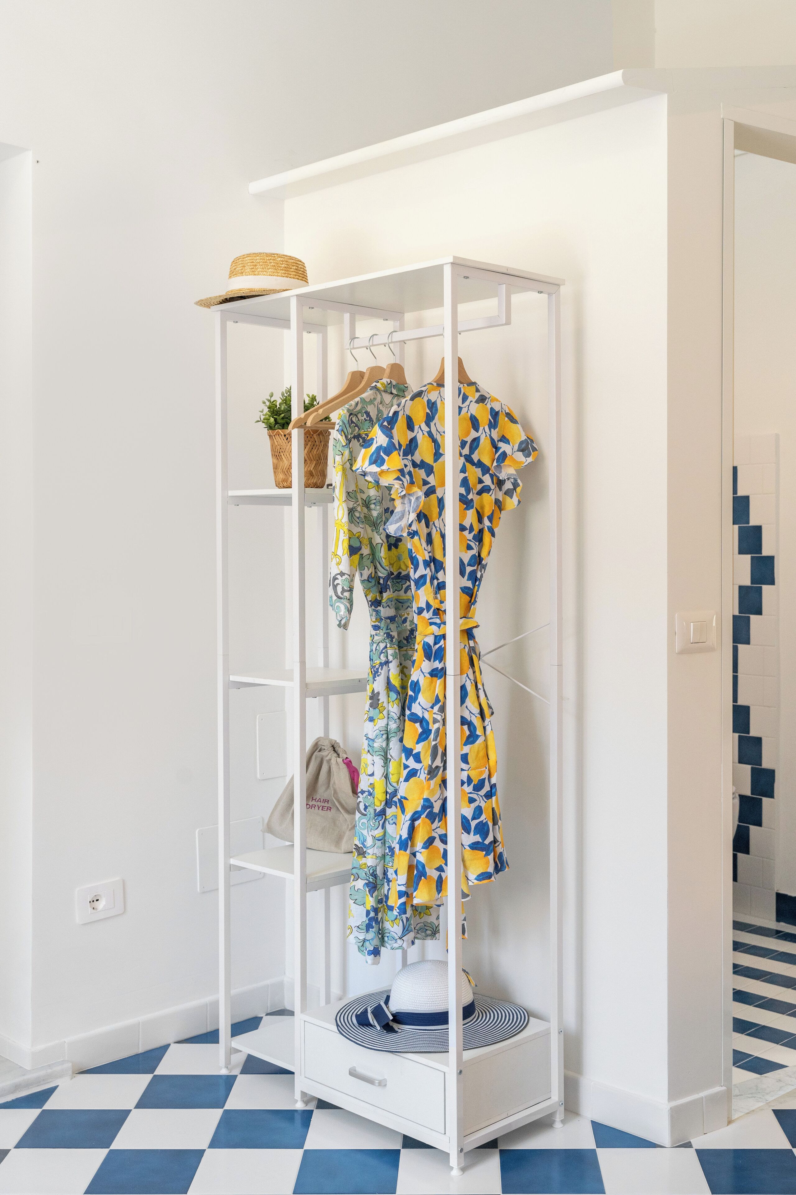 A white wardrobe with a dress on a hanger, a small plant, and a hat on top.