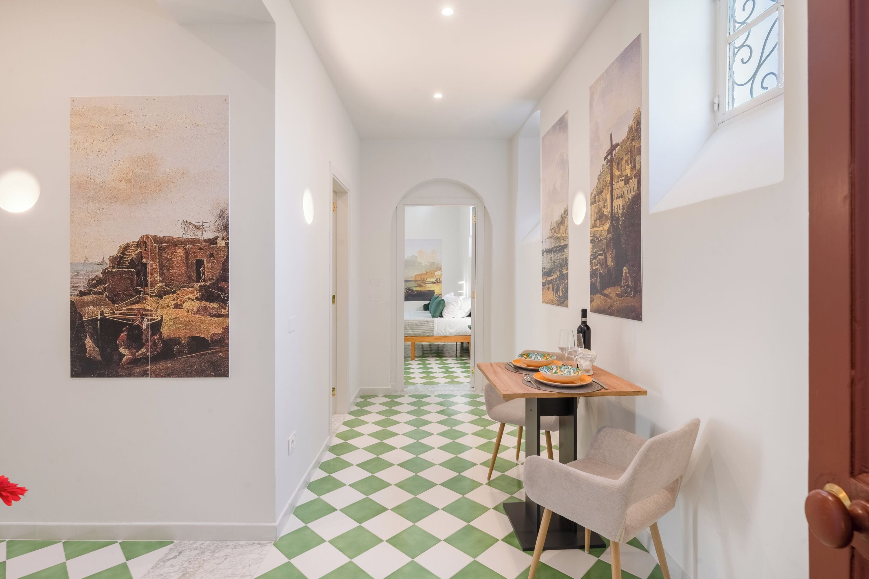 A hallway with a checkered floor, a dining area with a table set for two, and artwork on the walls.