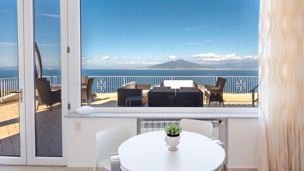 A balcony with a table and chairs, a view of the sea, and a mountain in the distance. - Villa With Panoramic Vesuvius And Sorrento Views With Private Pool (Sorrento)