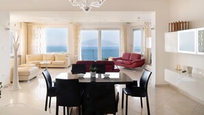 A spacious living room with a dining area, a red sofa, and a large window with a view of the sea. - Villa With Panoramic Vesuvius And Sorrento Views With Private Pool (Sorrento)