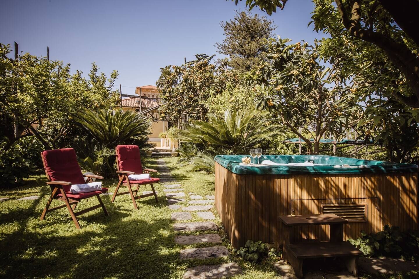 A garden with a hot tub, two red chairs, and a stone pathway.