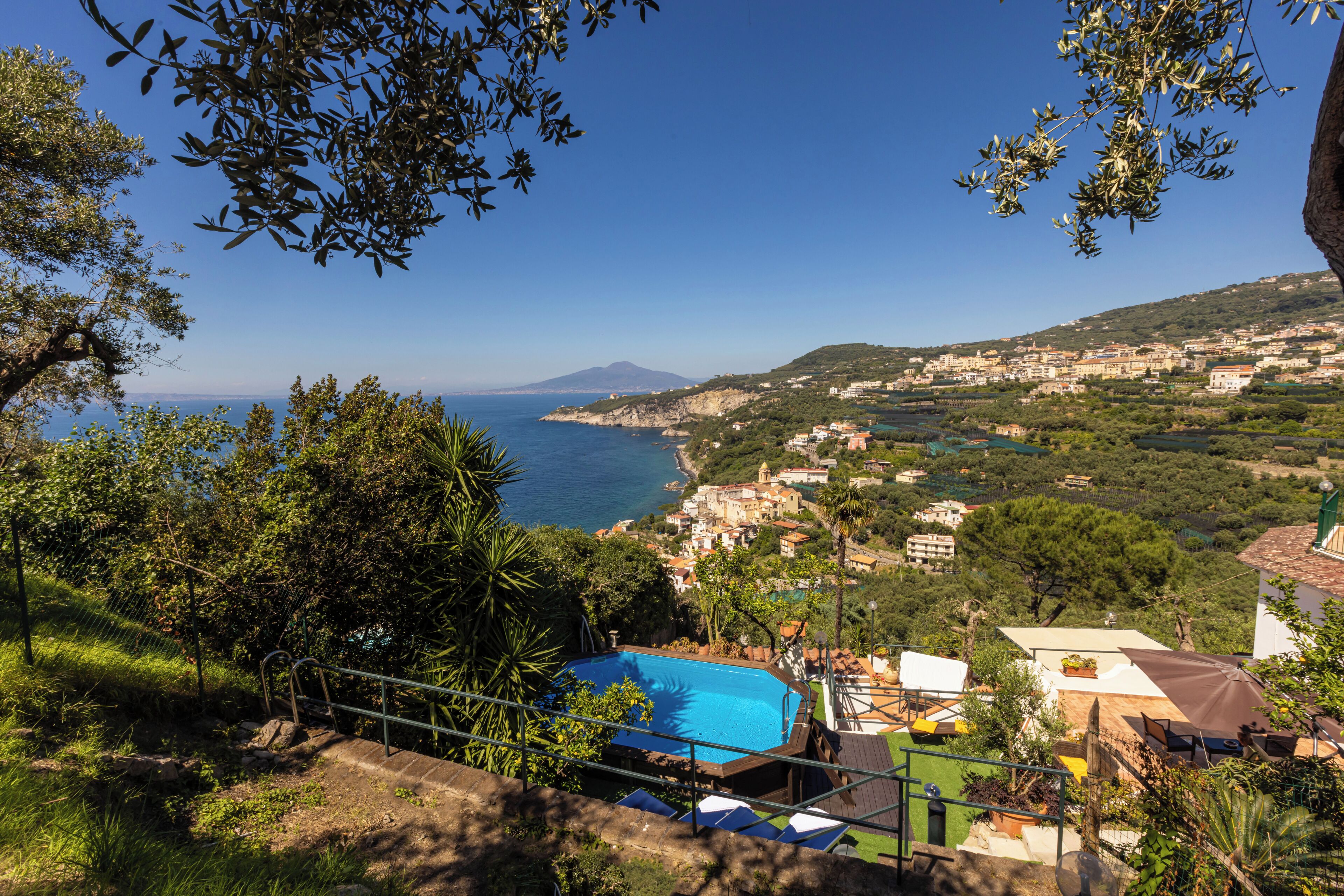 Vista costera con piscina, escaleras que bajan al agua y un pueblo al fondo.