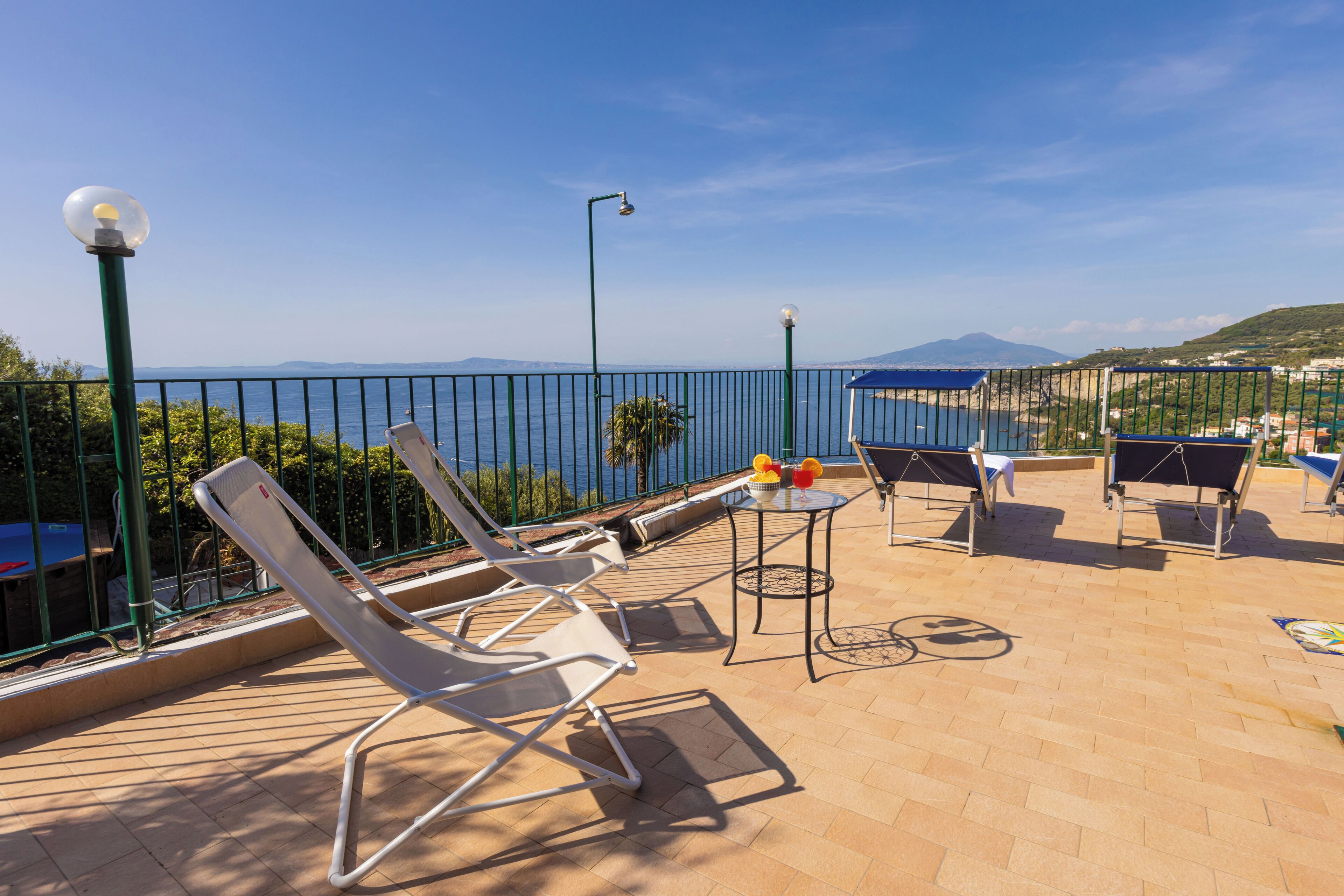 A terrace with lounge chairs, a table with a bowl of fruit, and a view of the sea.