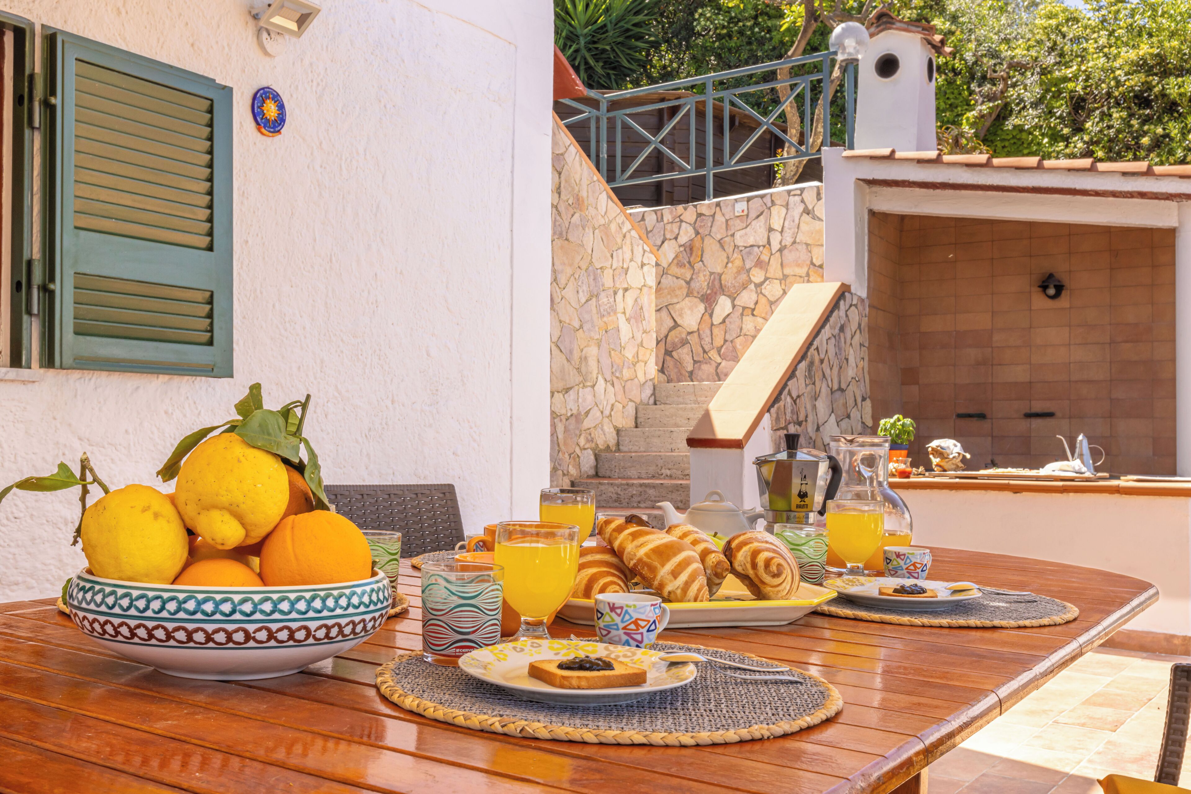 Une table de petit-déjeuner avec un saladier de fruits, des croissants et du jus d’orange.