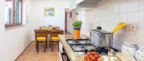 A kitchen with a gas stove, wooden chairs, a dining table, and a window with a view.