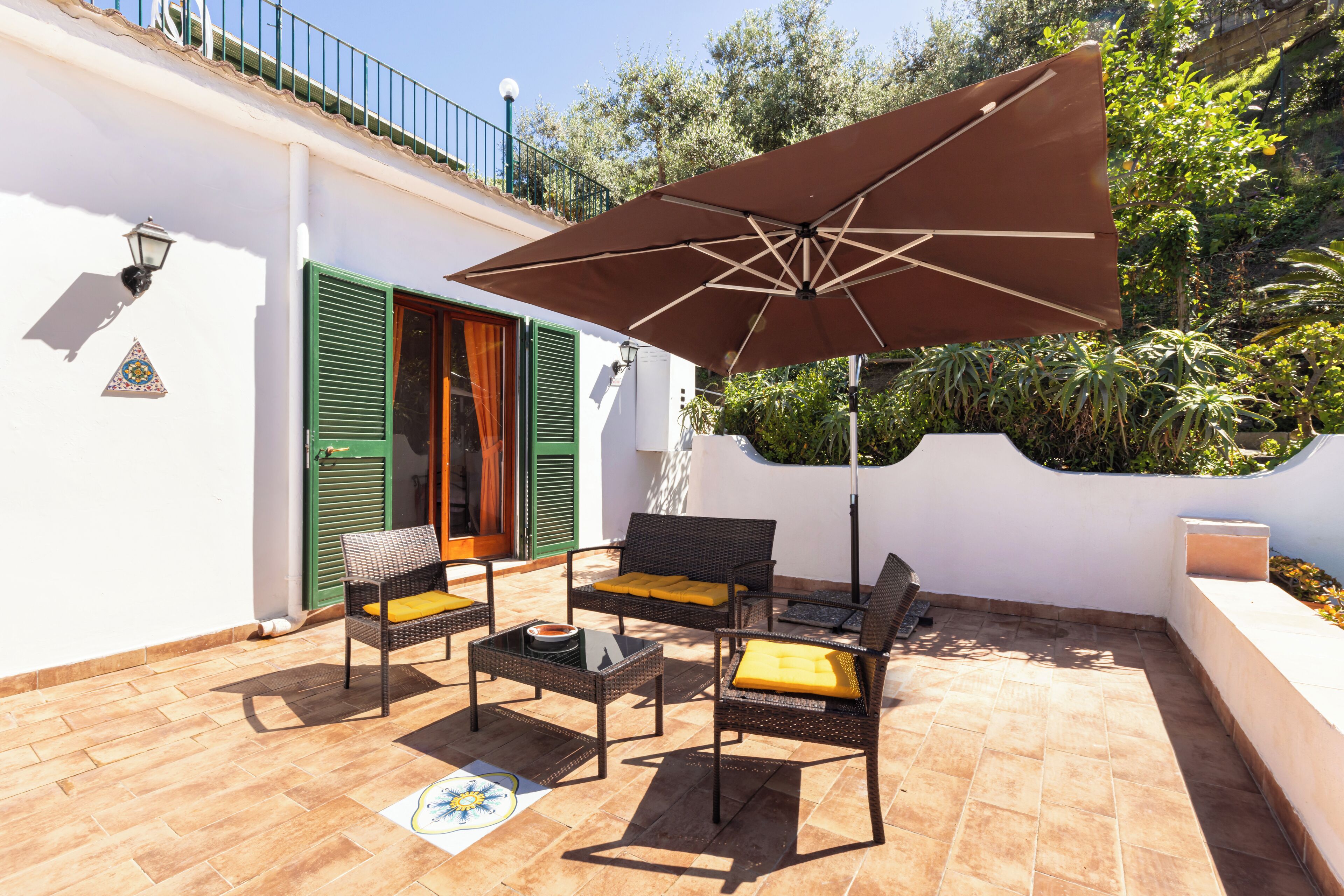 Un patio exterior con mobiliario de mimbre, un paraguas grande y suelo de baldosas.
