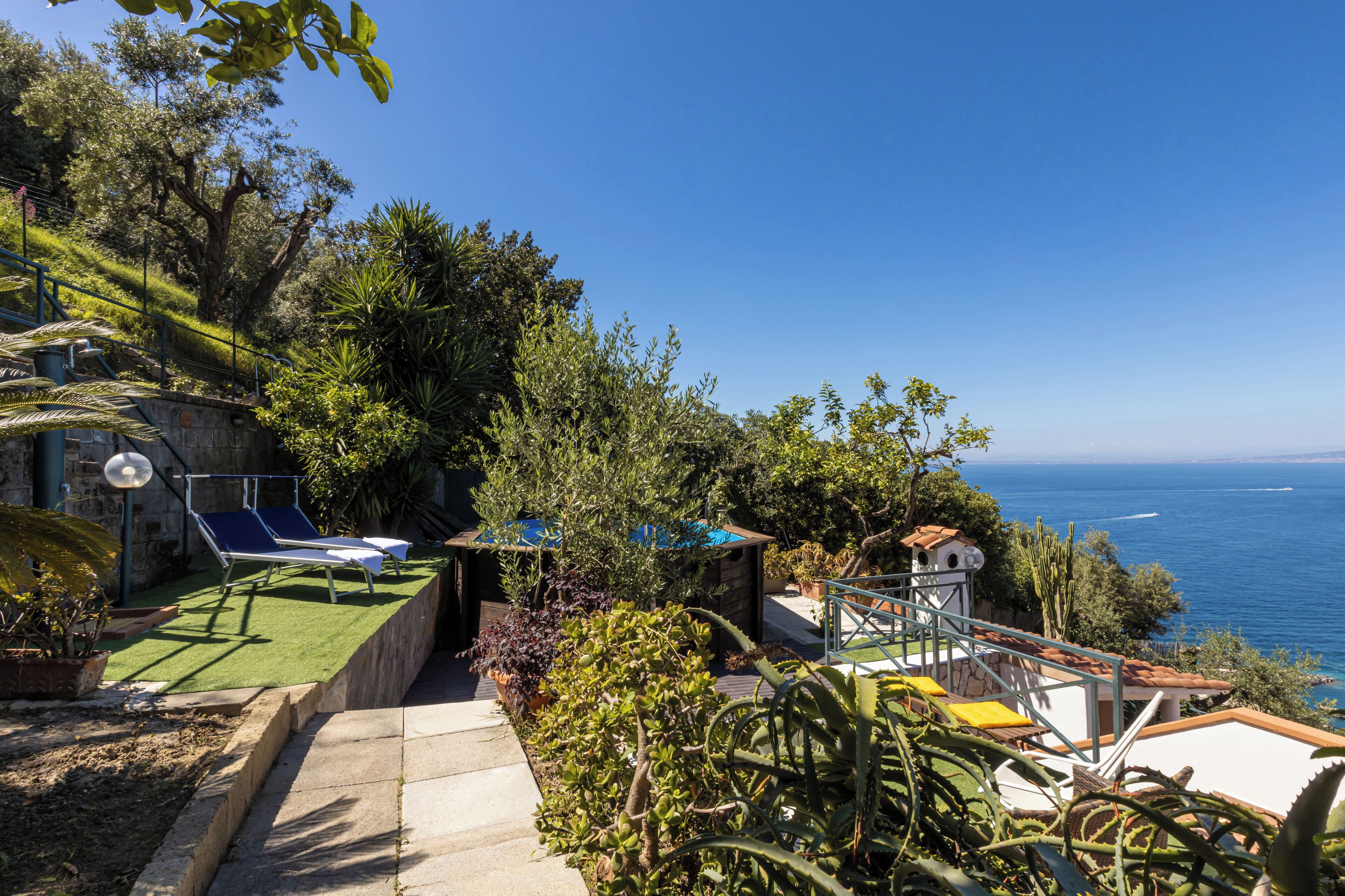 A terrace with a view of the sea, a small garden, and a seating area with a table and chairs.