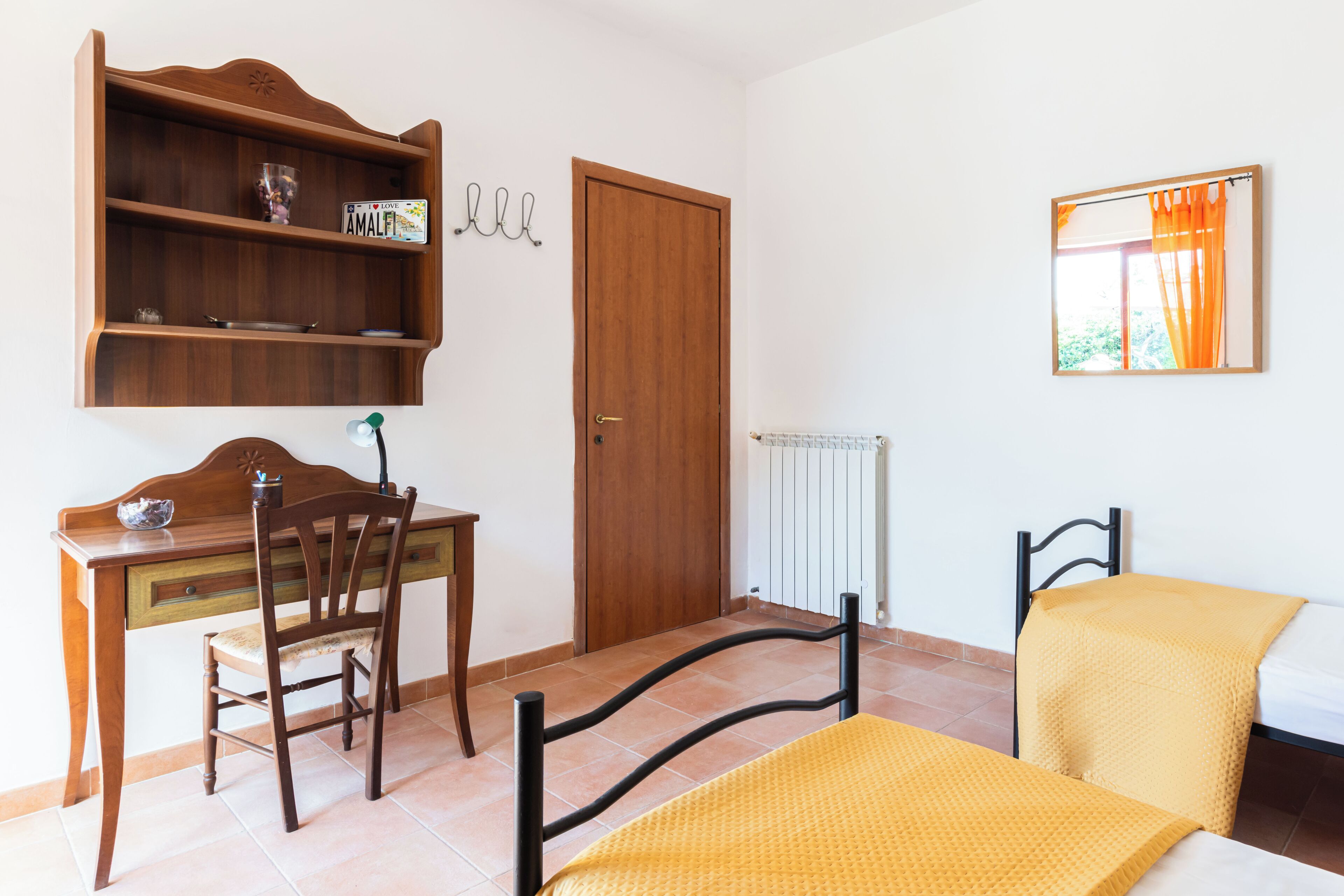 A bedroom with a wooden desk, chair, bed, and a radiator.
