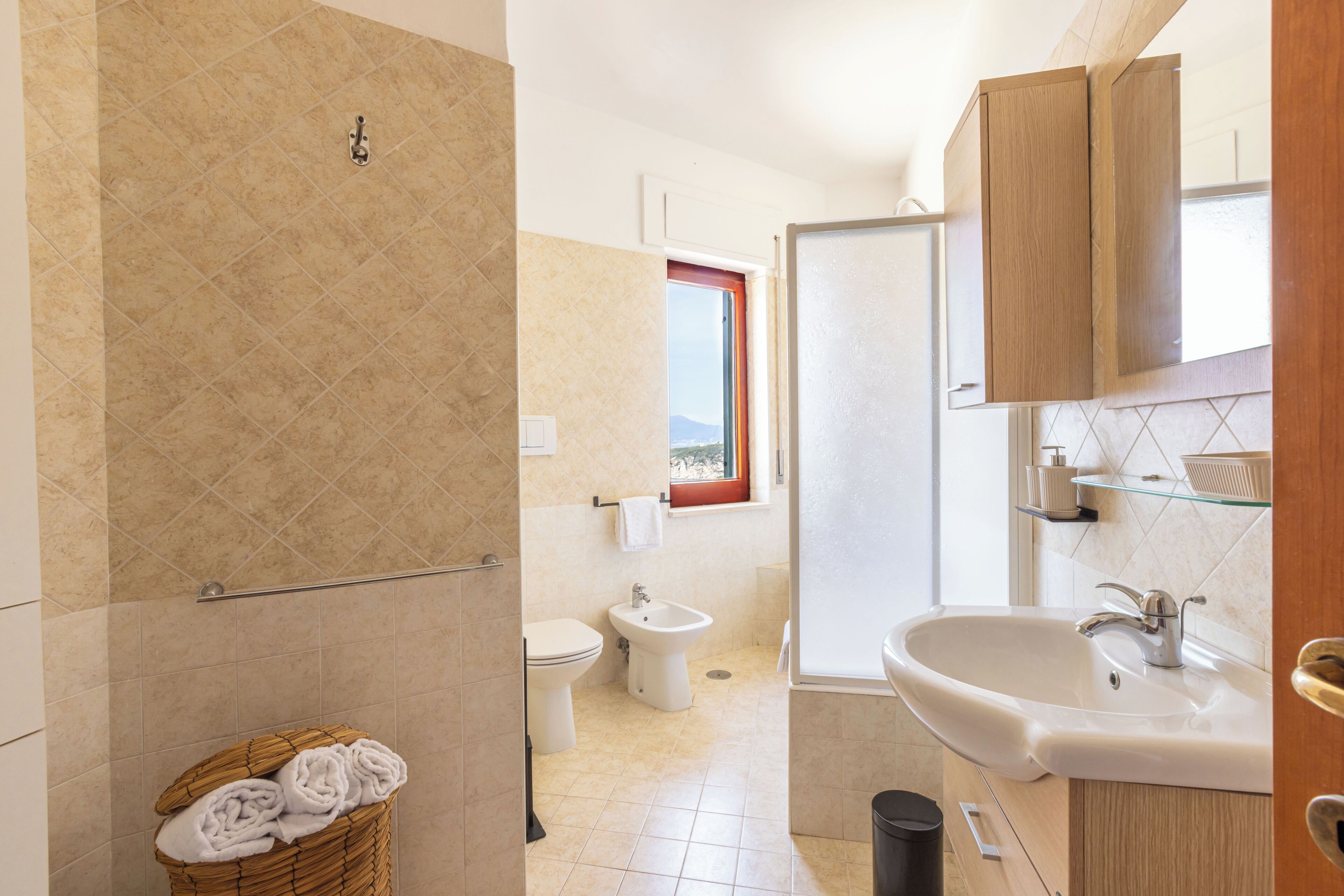 Een badkamer met toilet, bidet, wastafel en een raam met uitzicht.