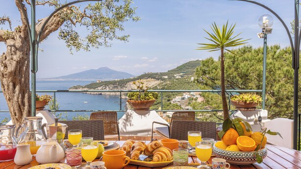 A breakfast table with croissants, orange juice, and a scenic view of the sea and mountains. - Villa Panorama With Private Pool & View (Massa Lubrense)