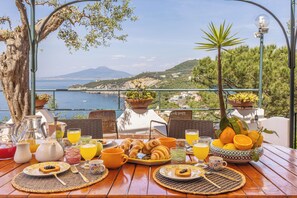 Een ontbijttafel met croissants, sinaasappelsap en een prachtig uitzicht op zee en bergen.