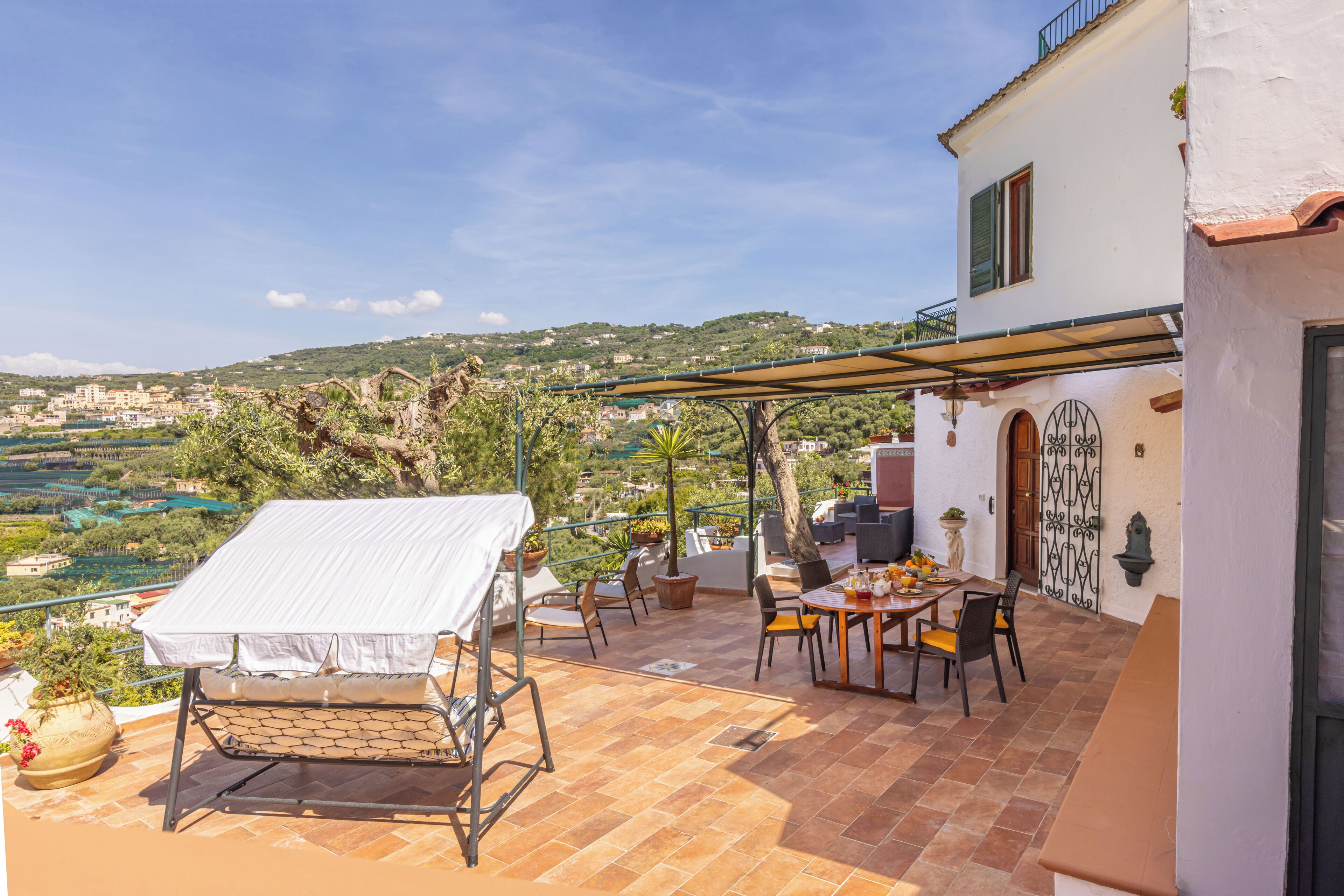 Une terrasse avec une table et des chaises, un espace salon couvert et une vue sur la campagne.