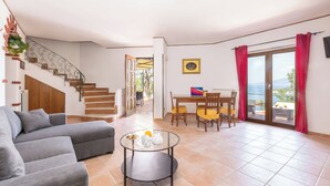 A living room with a sofa, a glass coffee table, a dining area with a table and chairs, a staircase, and a view through a glass door. - Villa Panorama With Private Pool & View (Massa Lubrense)