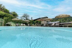A swimming pool with lounge chairs and umbrellas, surrounded by greenery and a building with a sloped roof. - Entire Hilltop Villa With Private Pool In Palazzuolo Sul Senio (Palazzuolo sul Senio)
