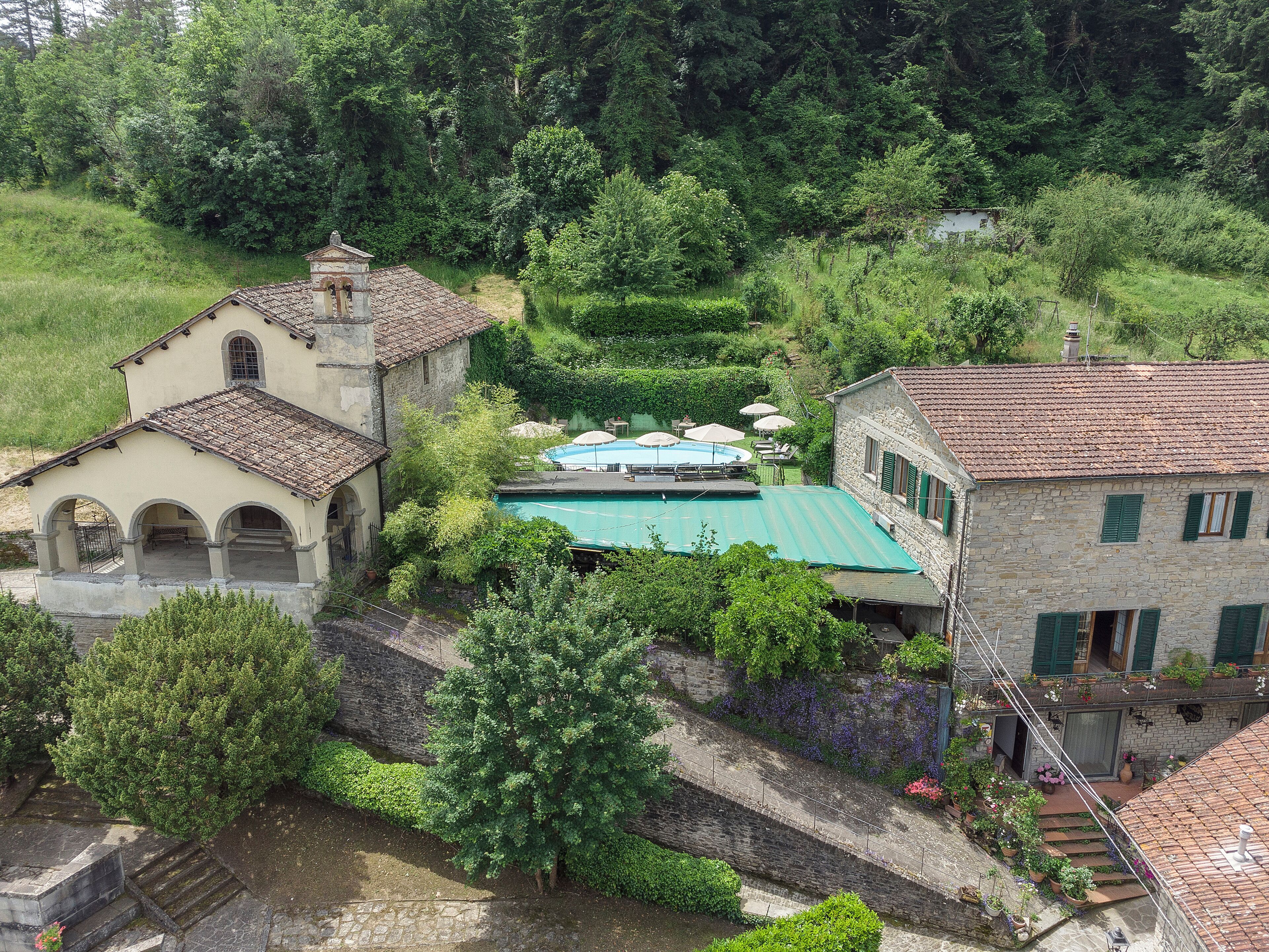 Un bâtiment traditionnel en pierre, doté d’une piscine, entouré d’une végétation luxuriante et agrémenté d’un pont en pierre.