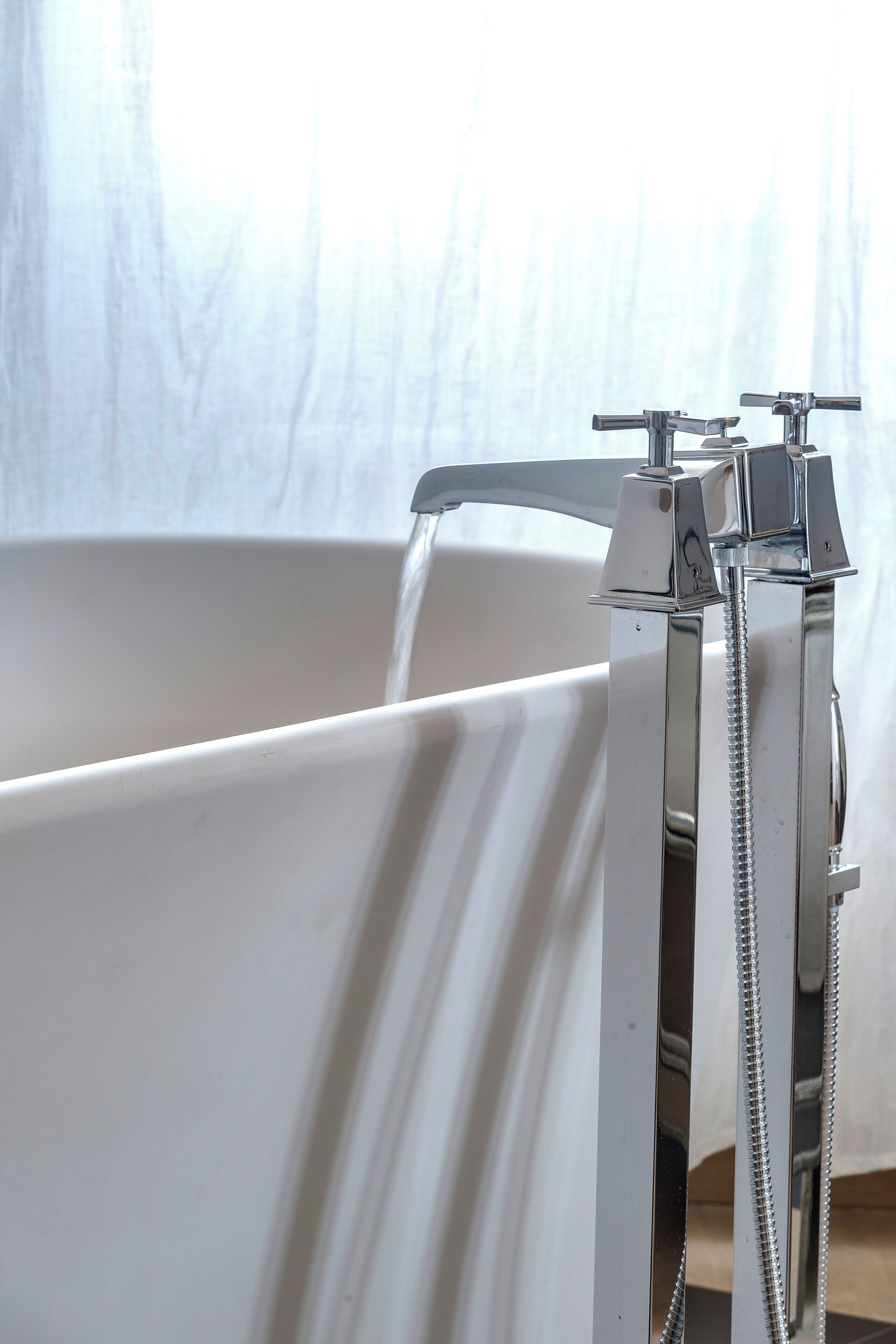 A bathtub with a chrome faucet and showerhead, a white curtain, and a visible water stream.