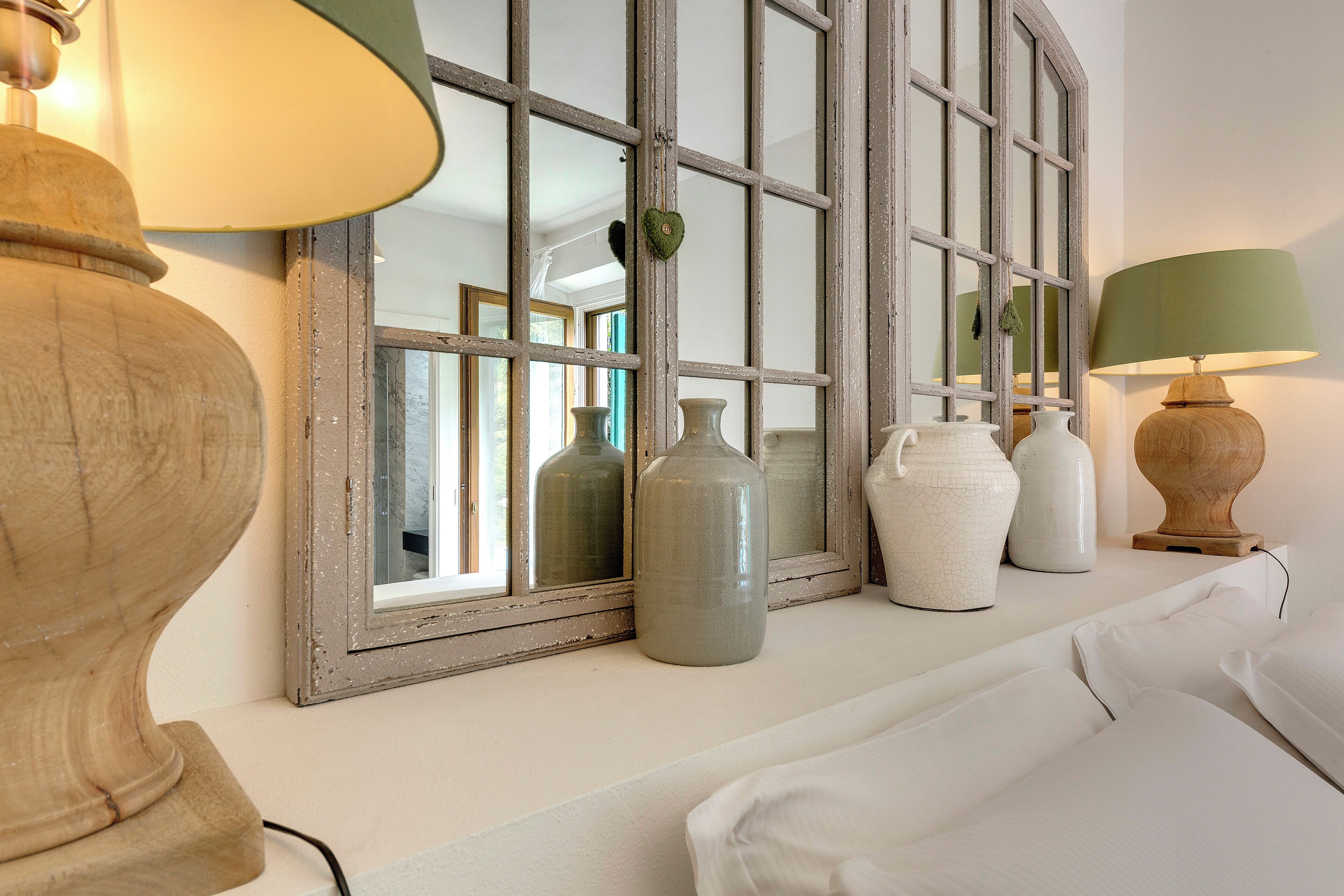 Una habitación con un espejo grande, un sofá blanco y varios jarrones en una estantería.