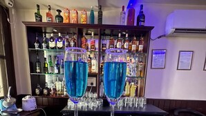A bar area with two glasses of blue cocktail on the counter, surrounded by shelves of various liquor bottles. - Hotel Anant Restaurant And Bar (Balh)