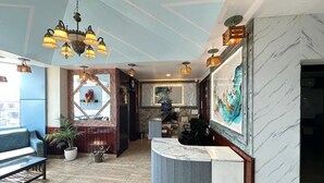 A modern lobby with a marble reception desk, a chandelier, and a large painting. - Hotel Anant Restaurant And Bar (Balh)