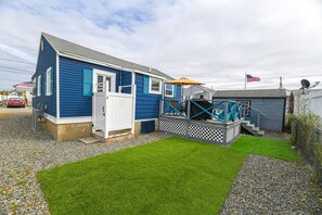 A blue house with a white door, a deck, and a small shed.