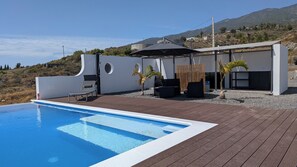 A modern outdoor pool area with a wooden deck, lounge chairs, and a covered seating area. - Villa PermaVista  with excellent climate zone (Tijarafe)