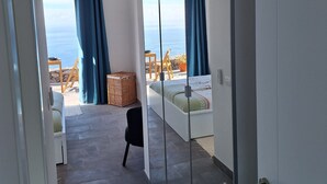 Een moderne kamer met een groot raam met uitzicht op zee, een bed, een stoel en een klein tafeltje met een mandje.