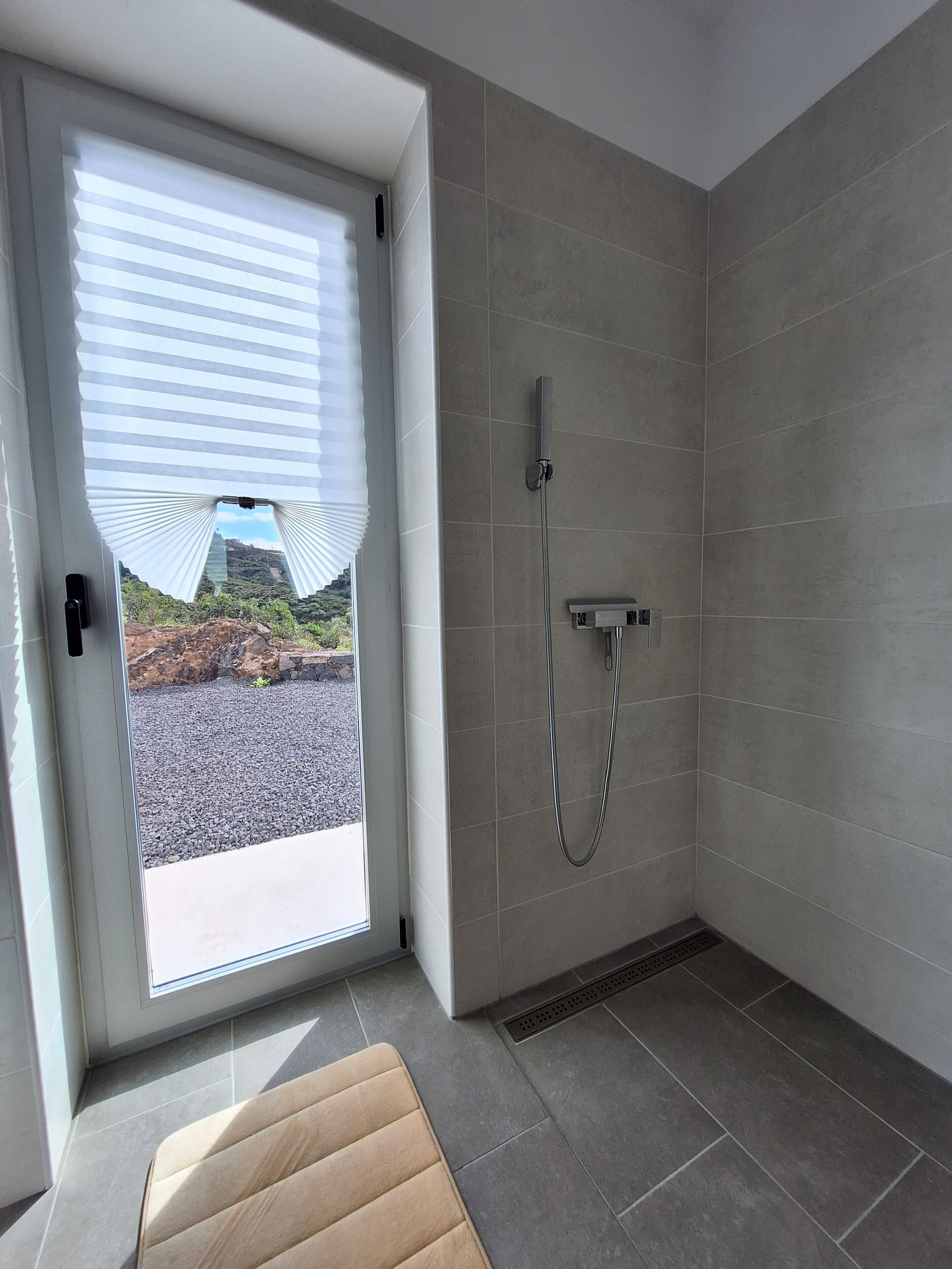 Ein modernes Badezimmer mit Dusche, Sitzbank und Blick auf eine felsige Landschaft durch eine Tür.
