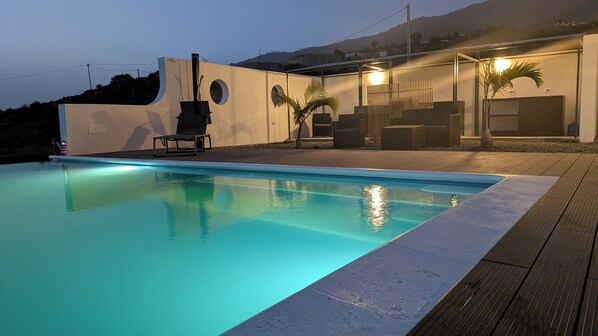 A swimming pool with a wooden deck, a modern building with a flat roof, and a mountain in the background. - Villa PermaVista  with excellent climate zone (Tijarafe)