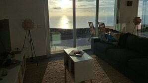 Een woonkamer met een grote schuifglazen deur die leidt naar een balkon met uitzicht op een wateroppervlak.
