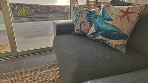 Een kamer met uitzicht op de oceaan, een grijze bank met een decoratief kussen en een houten stoel.
