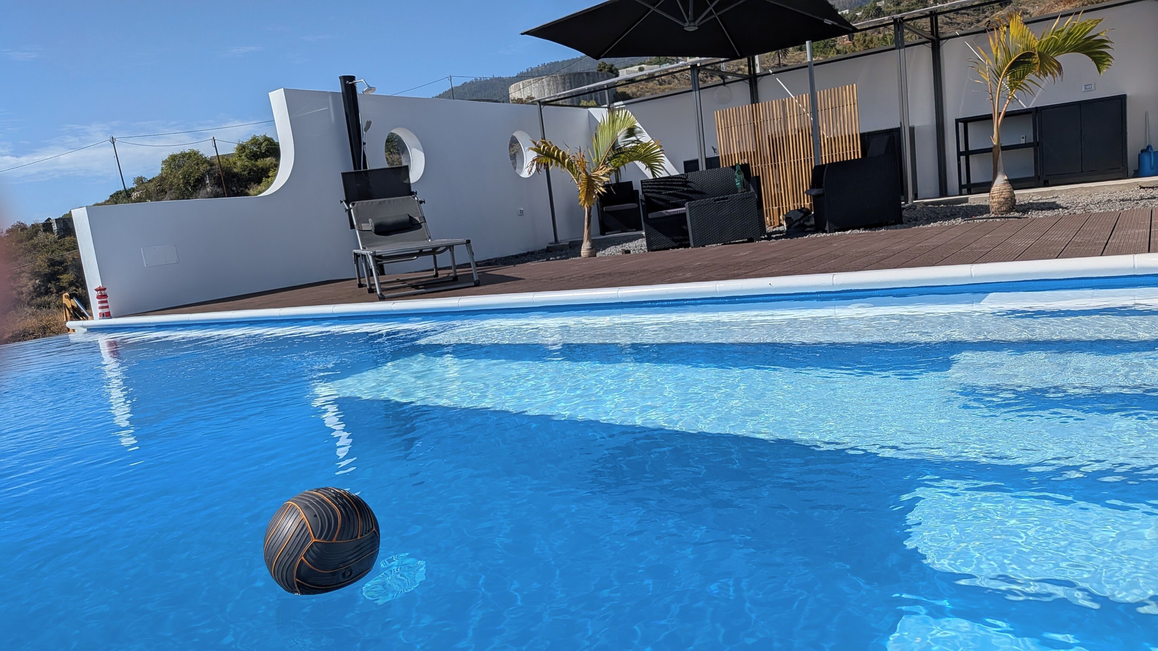 Una piscina amb una pilota de vòlei, gandules i un edifici modern de disseny arquitectònic singular.