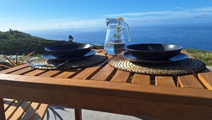 Een houten tafel met twee zwarte kommen en een glazen karaf met kruiden, met een prachtig uitzicht op de oceaan.