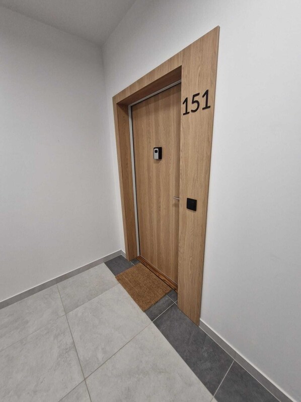 Un pasillo con una puerta de madera marcada con el número 151, un felpudo y un suelo de baldosas.
